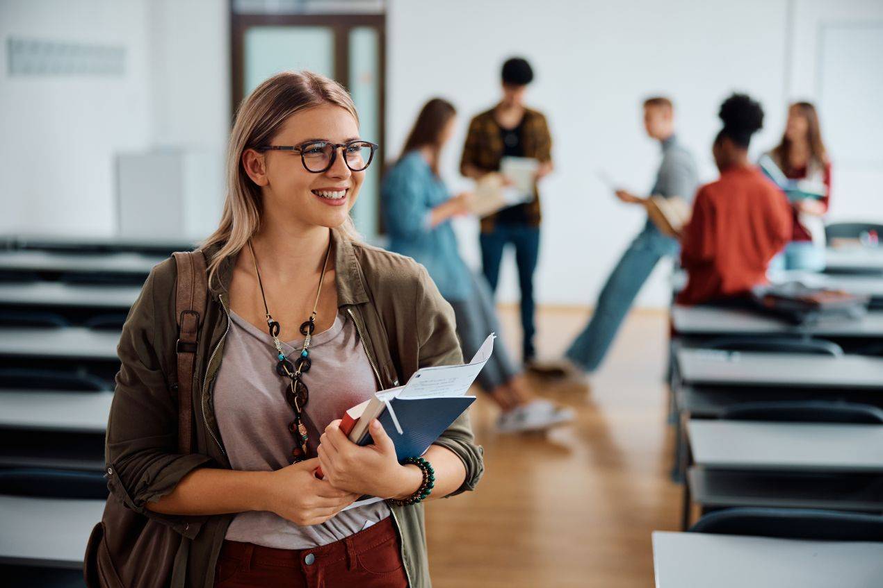Laechelnde studentin haelt buecher und notizen im seminarraum und nutzt tipps von ghostwriter bachelorarbeit experten